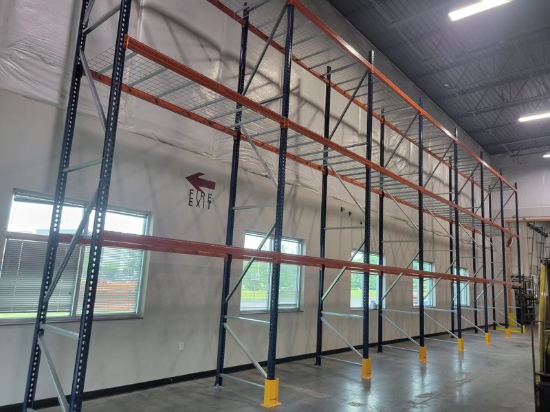 Selective pallet racking with blue uprights and orange beams along a warehouse wall