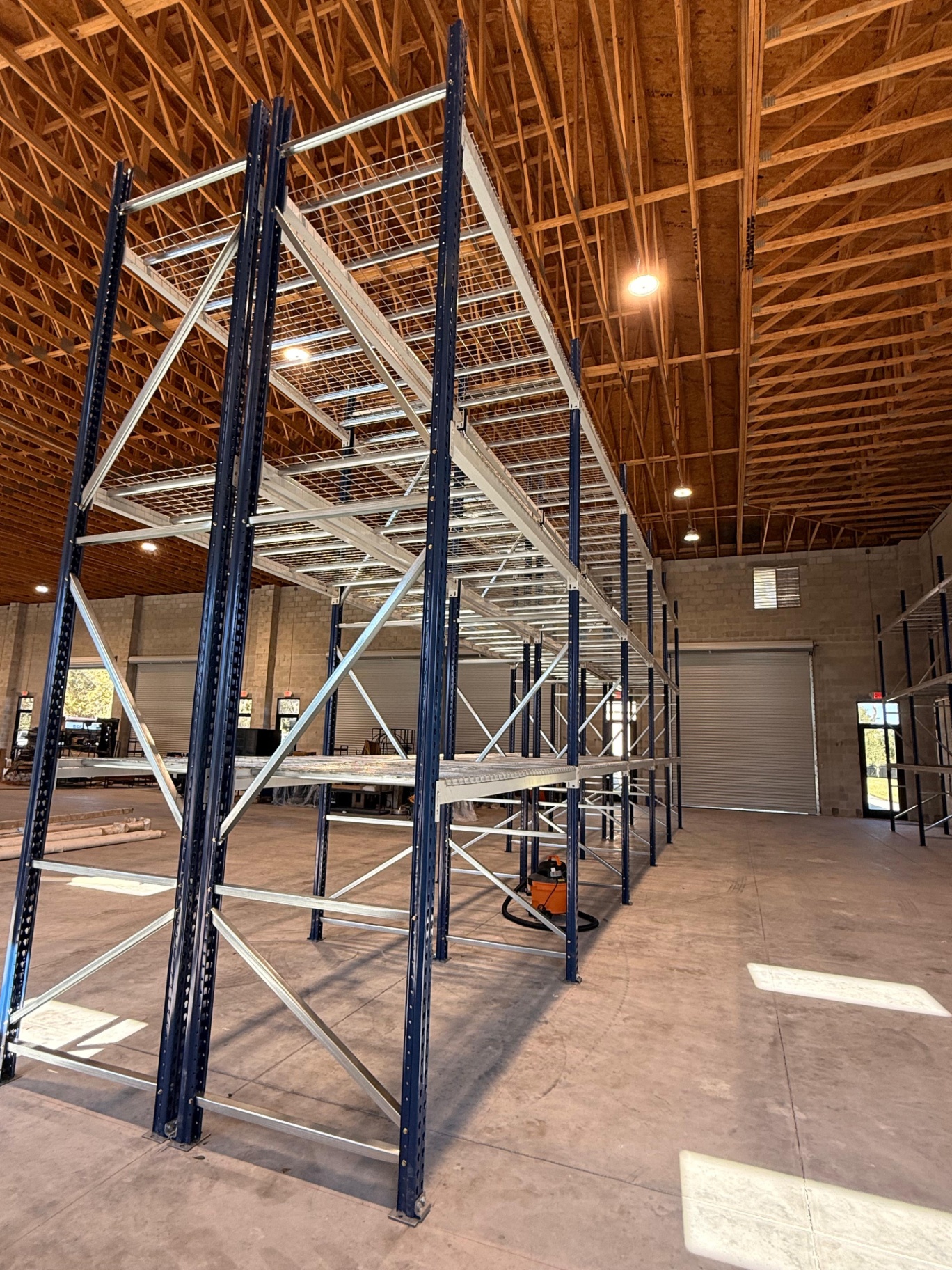 Selective pallet racking with blue uprights and wire decking under a wood-truss roof